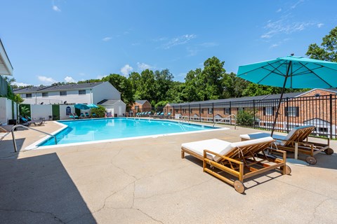 A pool with a sun lounger and umbrella in front of a building.