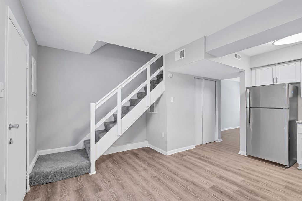 A white staircase with a grey carpet leads to a kitchen area.
