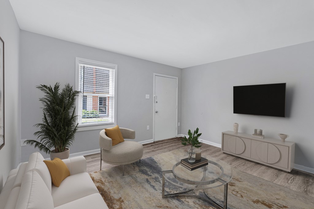 A living room with a white couch, a glass coffee table, and a flat screen TV mounted on the wall.