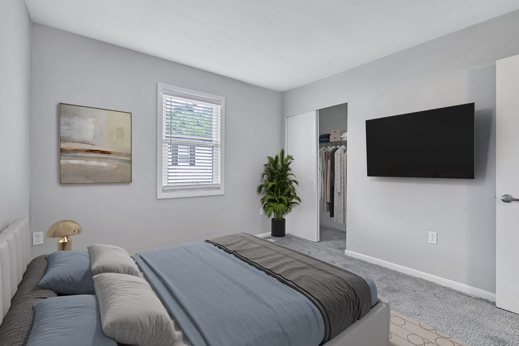 A bedroom with a bed, a plant, a painting, a window, and a door.