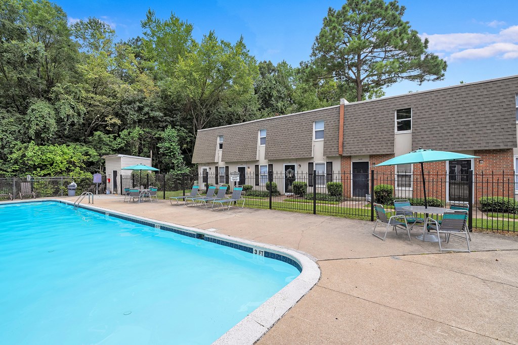 A swimming pool surrounded by chairs and trees.