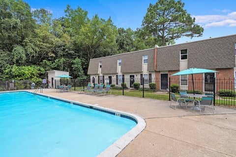 A swimming pool surrounded by chairs and trees.