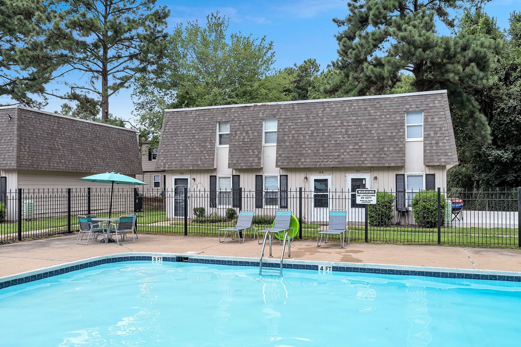 A swimming pool in front of a building with a fence and chairs around it.