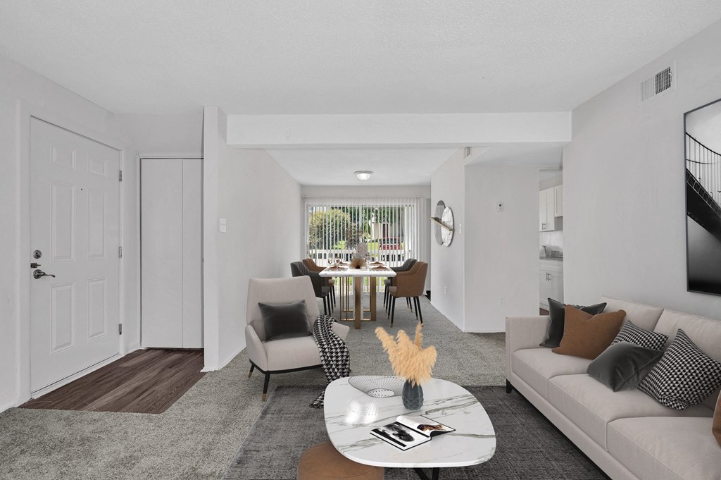 a living room with white walls and a large window with a view of a dining room