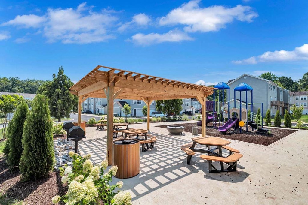 a picnic area with benches and tables and a playground in the background