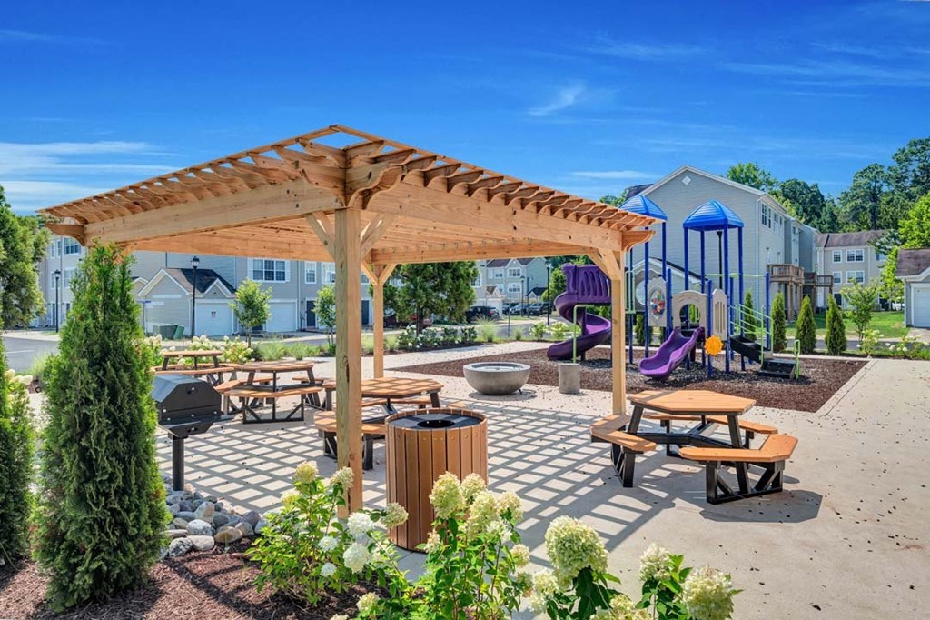 a picnic area with benches and tables with a playground in the background