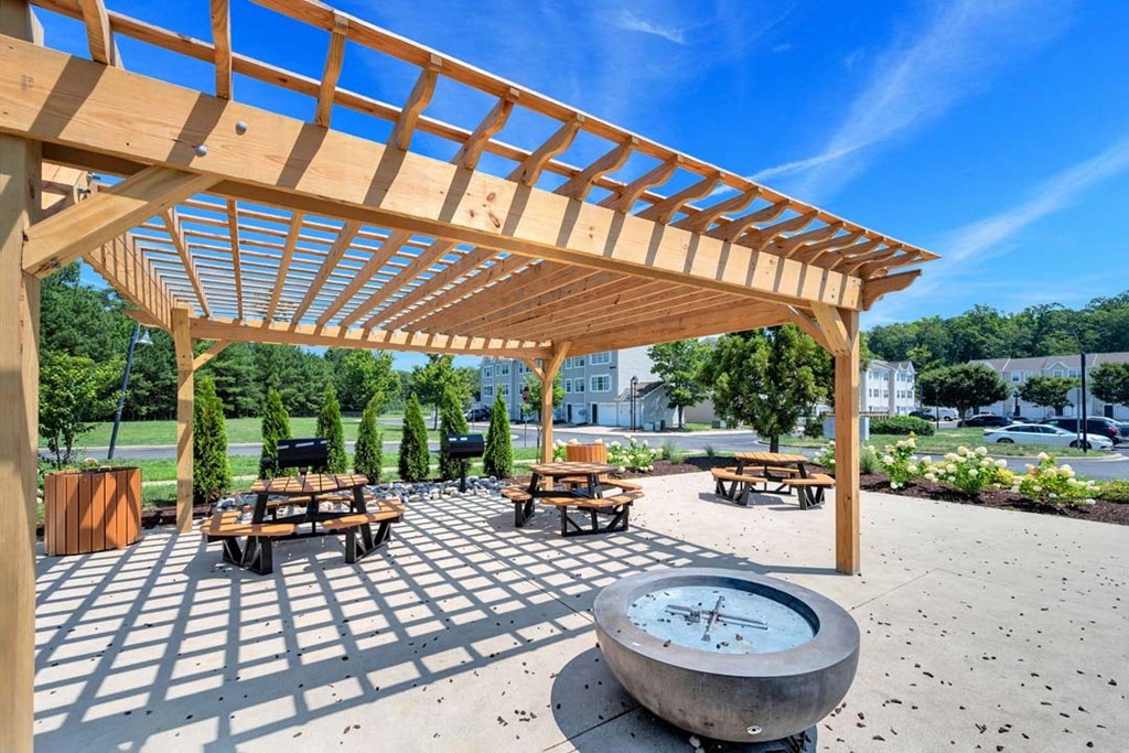 a fire pit and picnic tables under a wooden pergola with a blue sky in the