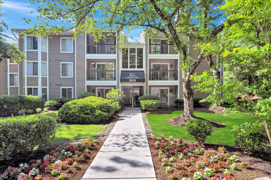 a walkway in front of an apartment building with trees and grass