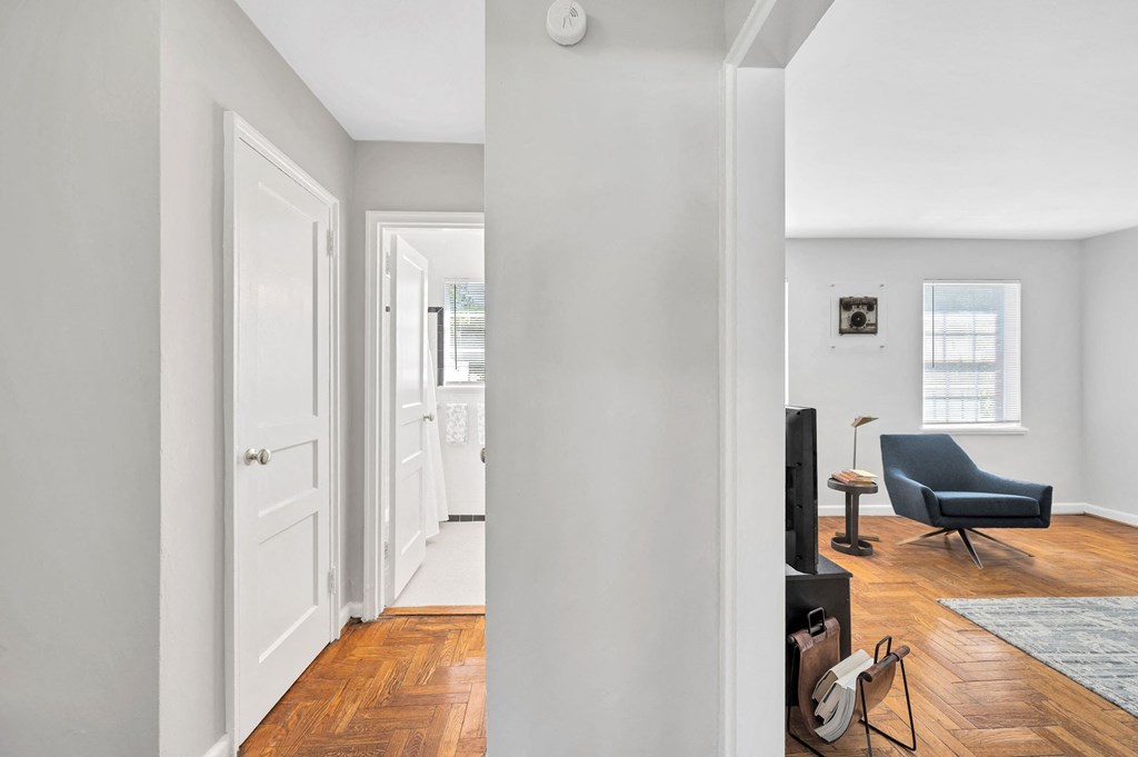 a living room with white walls and a door to a room with a black chair