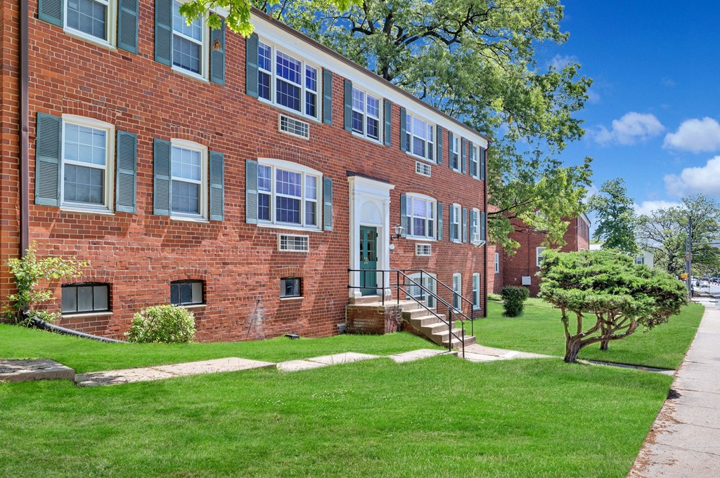 a red brick apartment building with green grass and a sidewalk