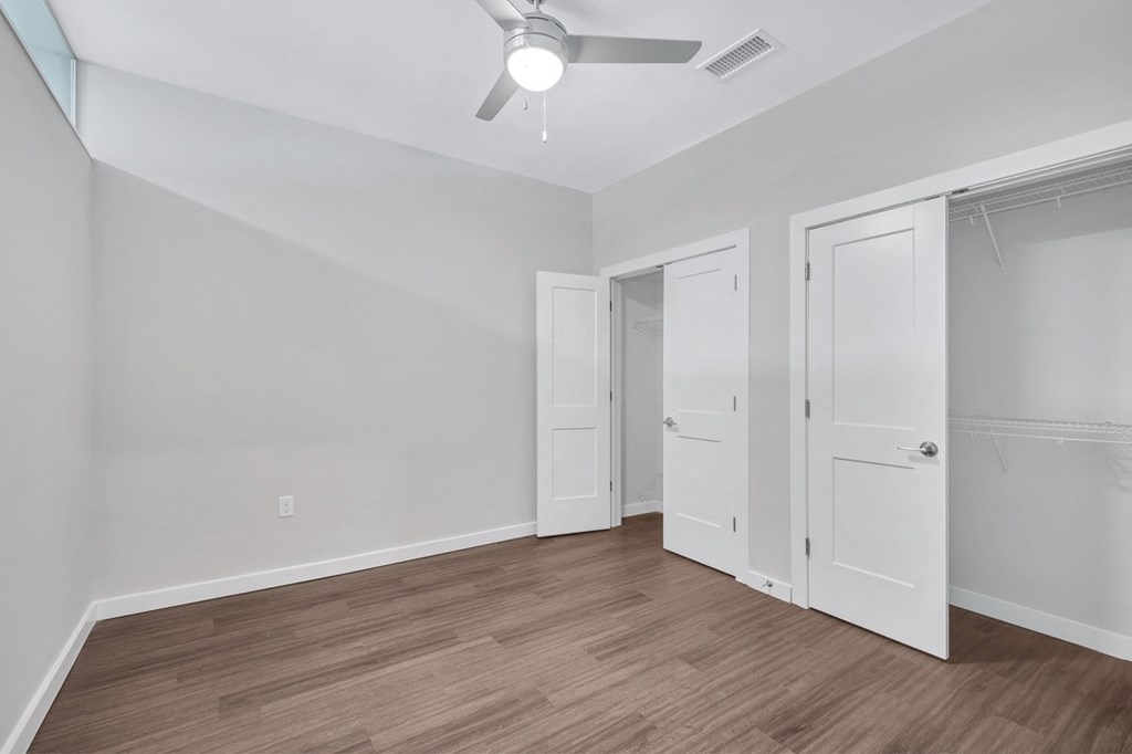 a bedroom with white walls and wood flooring and a ceiling fan