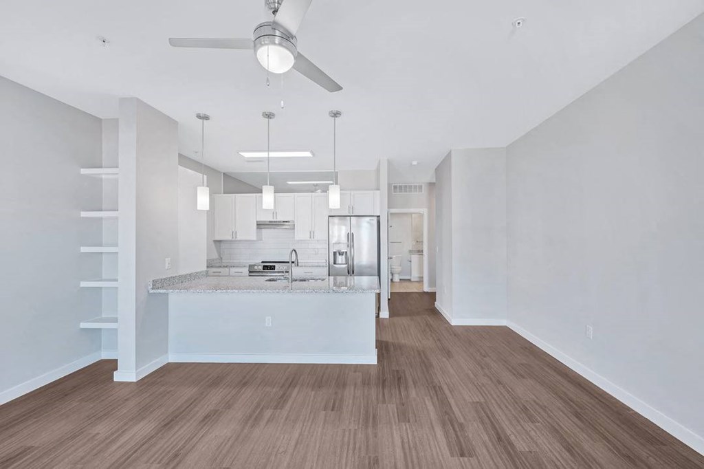 an empty living room with a kitchen and a ceiling fan