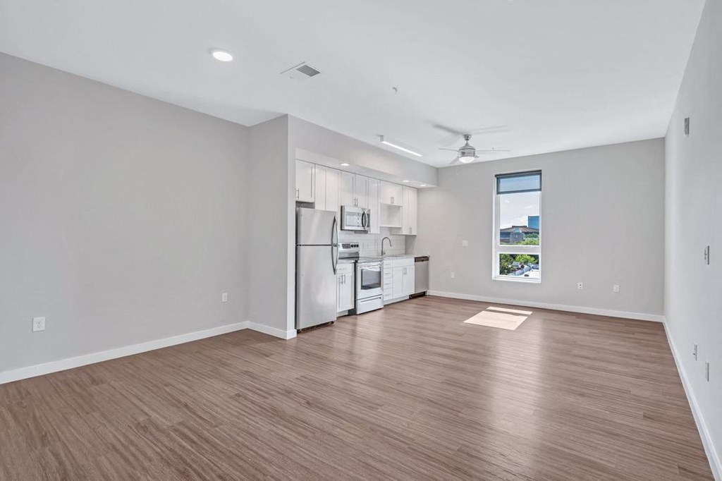 an empty living room with a kitchen and a window