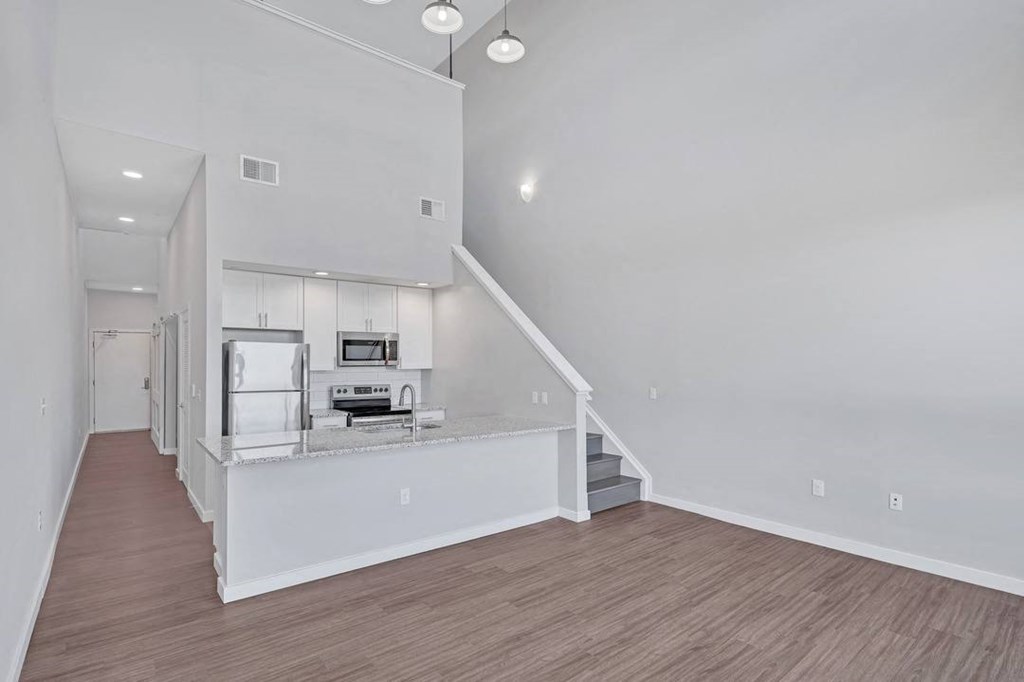 an empty living room with a kitchen and a staircase
