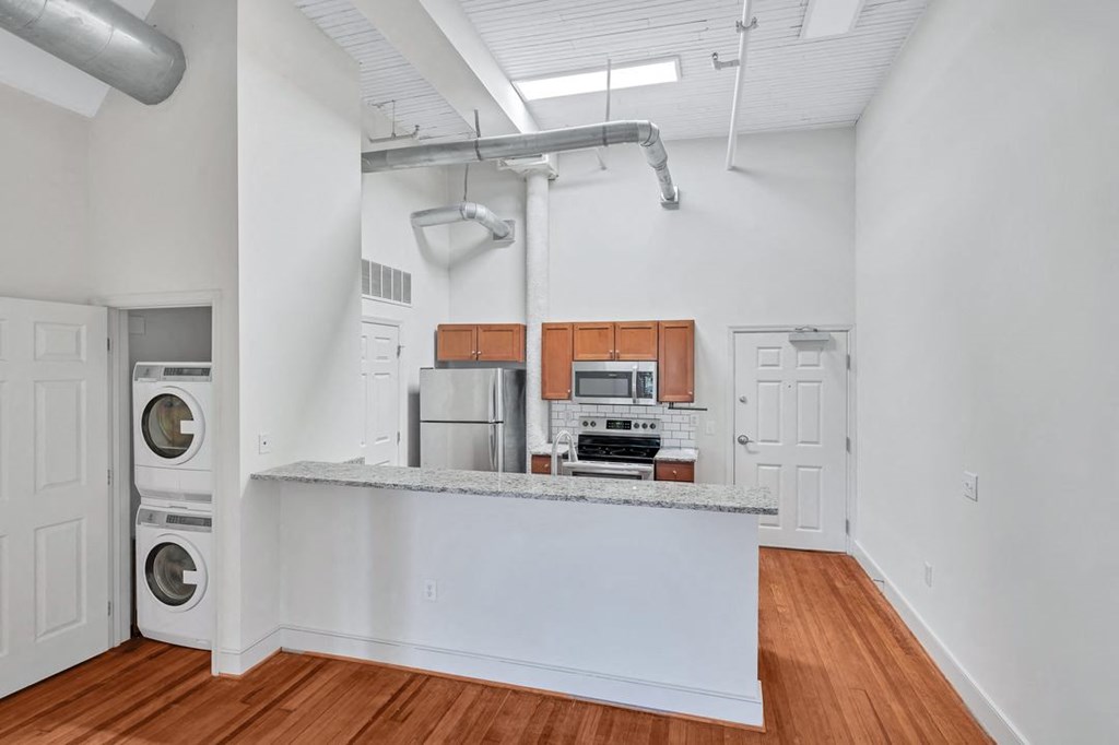 a studio apartment shows kitchen with a counter top and a washer and dryer and exposed pipes.