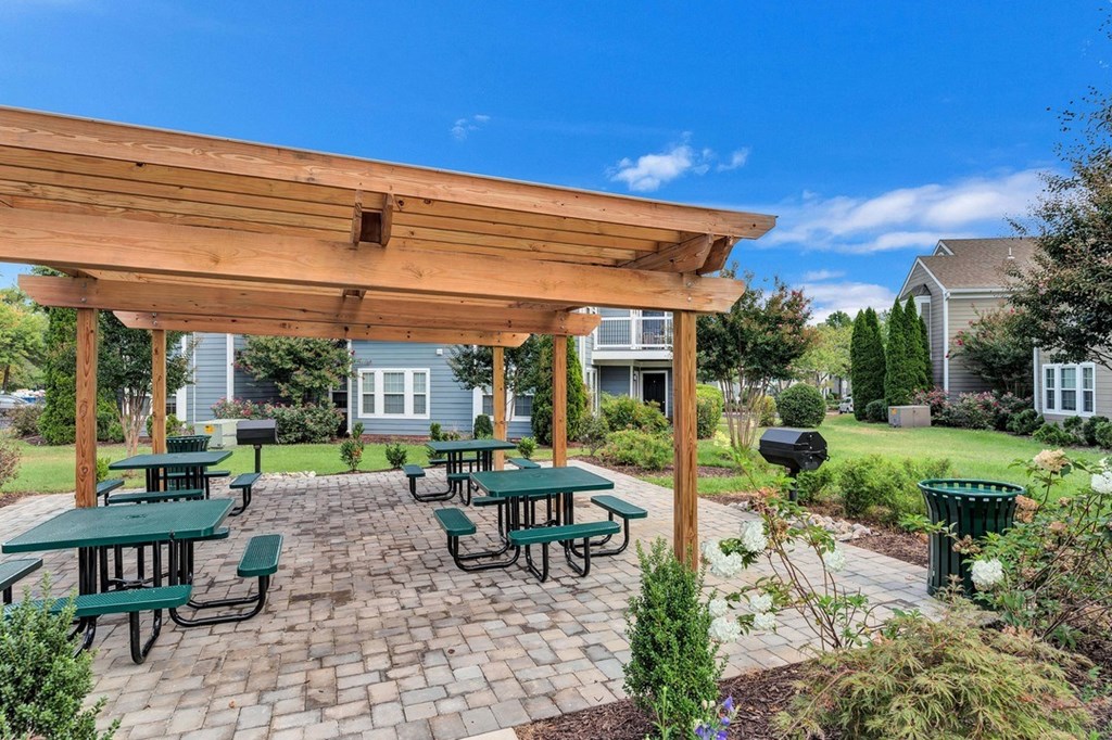 a cobblestone picnic area with seating and pergola.
