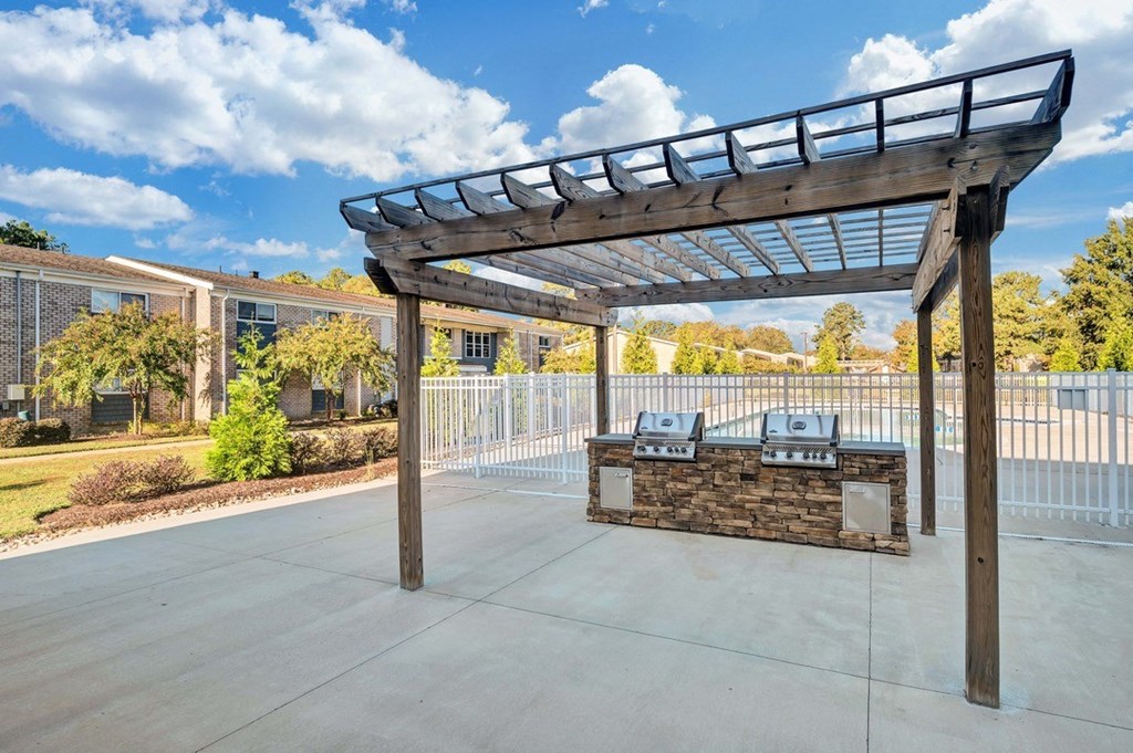 a patio with a grill and a pergola with a blue sky in the background