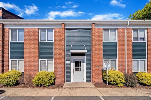 a brick building with a white door and green bushes in front of it