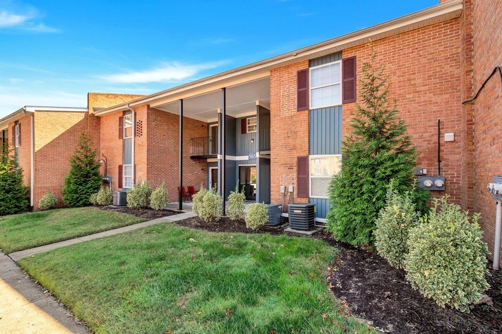 a brick building with a green lawn and trees in front of it