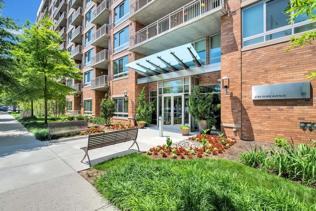 a bench in front of an apartment building with a sidewalk and grass