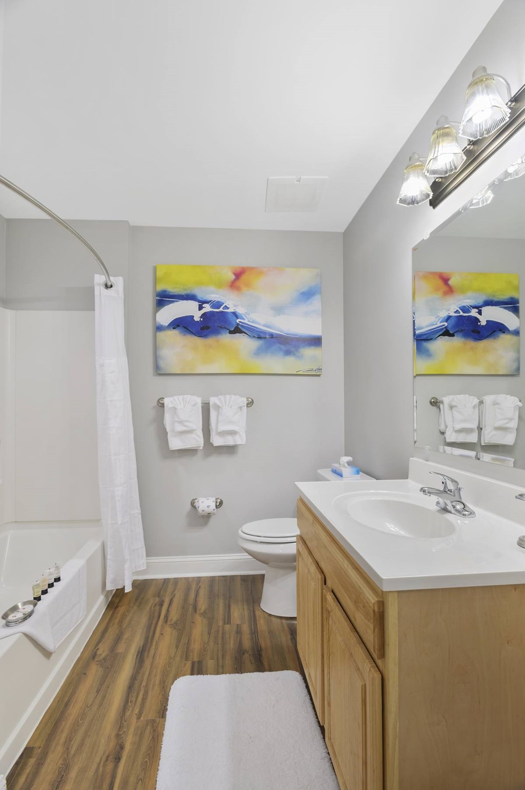 A bathroom with a wooden vanity and a painting above the toilet.