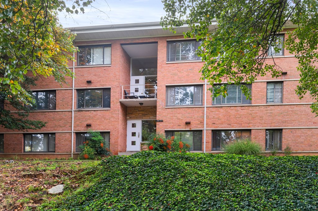 the exterior of a brick apartment building with trees and bushes