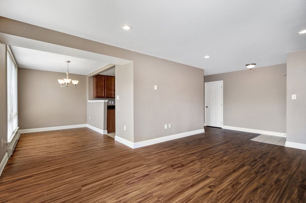 an empty living room with wood flooring and a kitchen