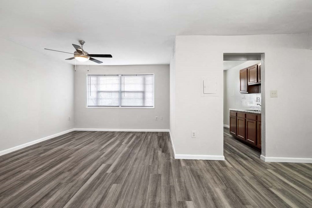 an empty living room with a ceiling fan and a kitchen