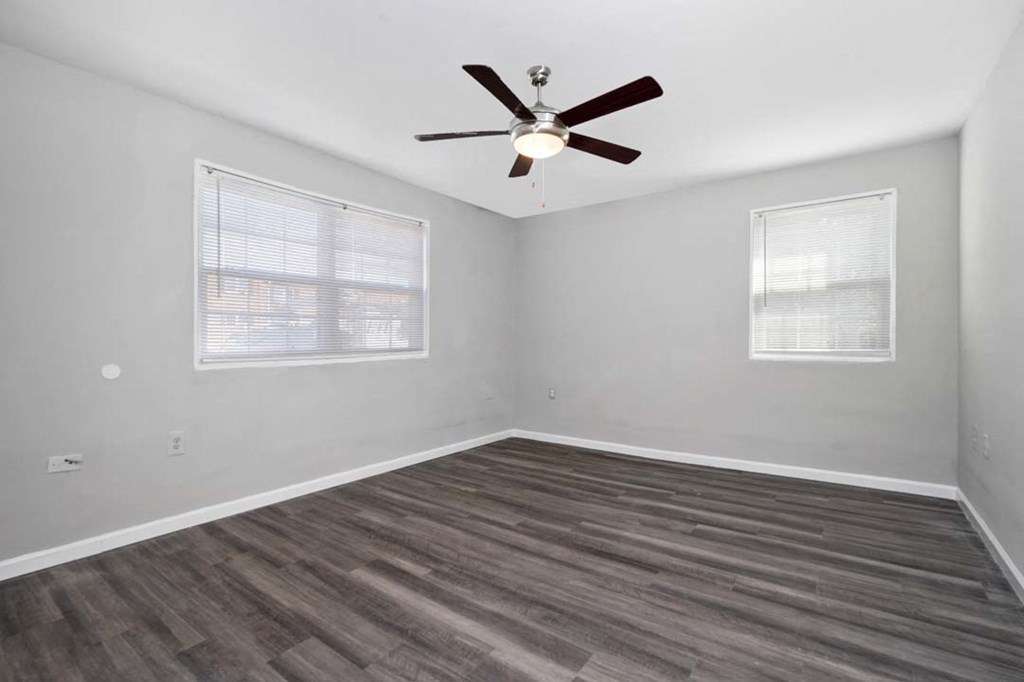 an empty room with a ceiling fan and two windows