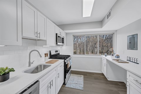 A kitchen with white cabinets and a window overlooking trees.