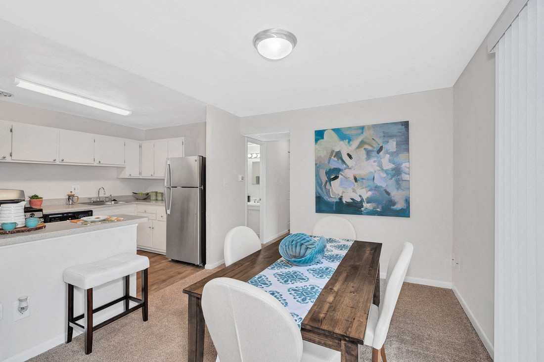 a dining room with a table and chairs and a kitchen in the background