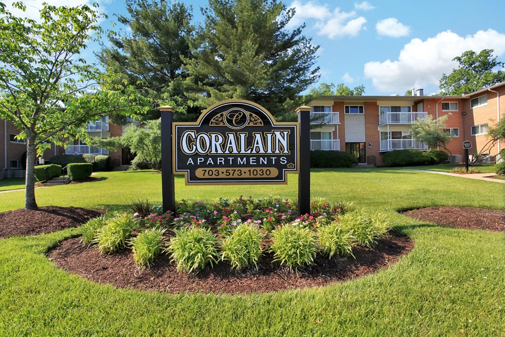 a sign for coral apartments in front of a yard with flowers