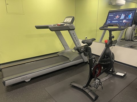 A treadmill and a stationary bike are in a gym.