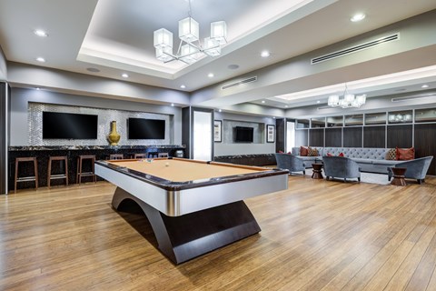 A pool table is in the middle of a room with a bar and a couch.