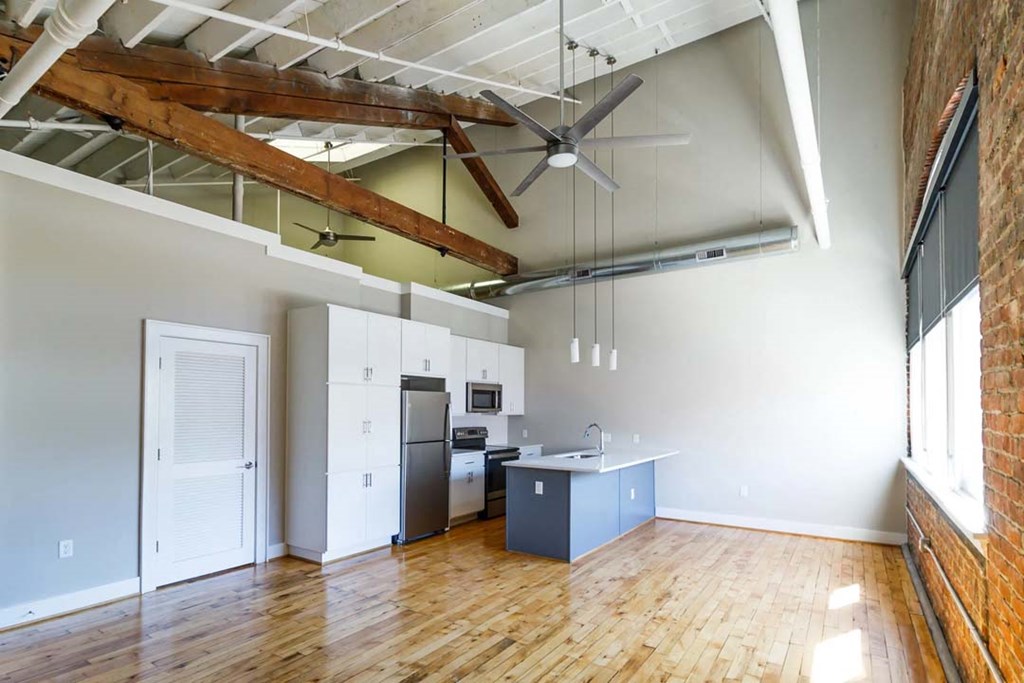 an empty living room with a kitchen and a ceiling fan