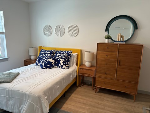 A bedroom with a bed, nightstand, and a dresser with a mirror on top.