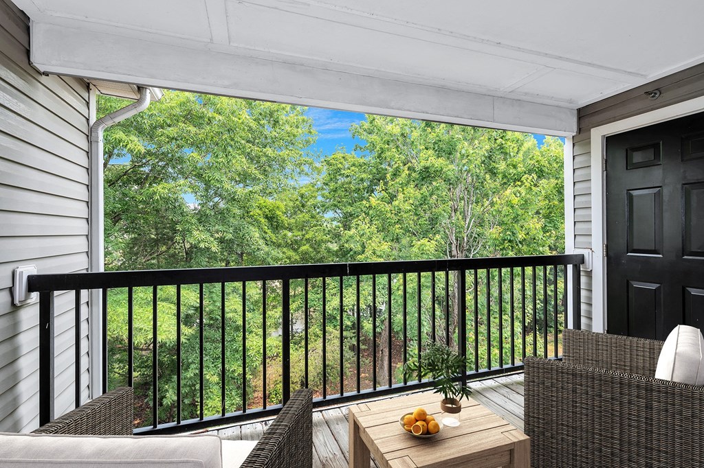 View from furnished balcony to lush wooded landscape.