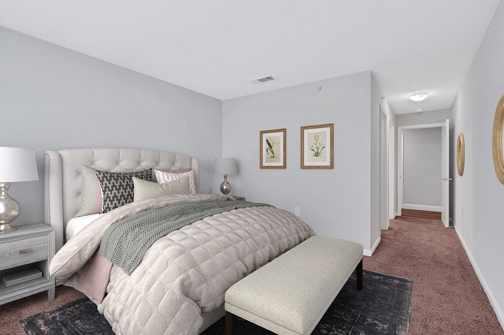A spacious apartment bedroom with large bed and bench at the foot and hallway to closet and bathroom.