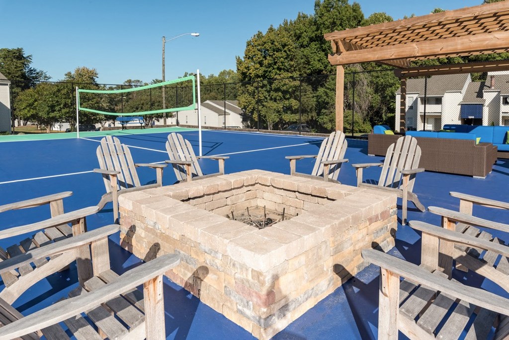 a fire pit with chairs and a volleyball court in the background