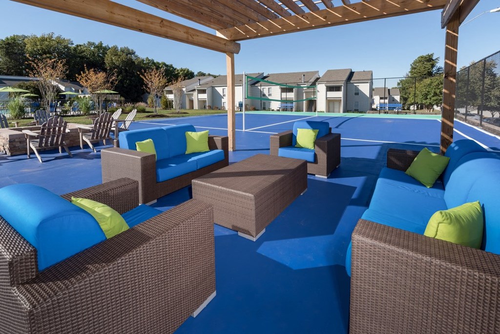 a lounge area with blue couches and green pillows on top of a blue tennis court