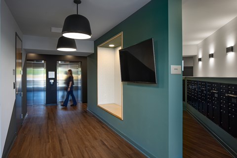 A hallway with a person walking in the distance and a TV mounted on the wall.