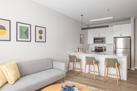 A modern living room with a grey couch and a kitchen area in the background.