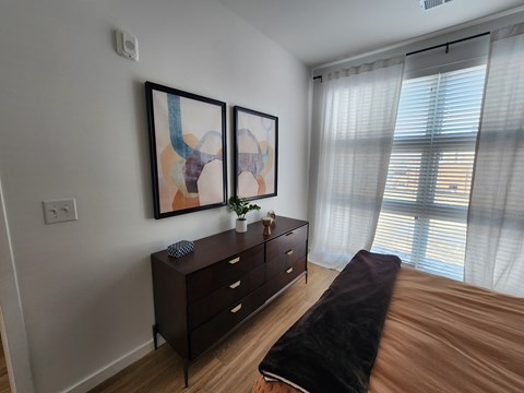 A bedroom with a brown bed, a brown dresser, and two framed artworks on the wall.