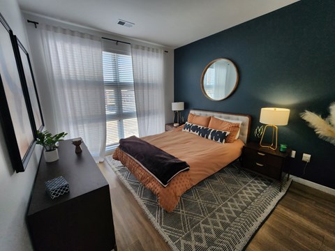A bedroom with a bed, nightstand, and a round mirror on the wall.