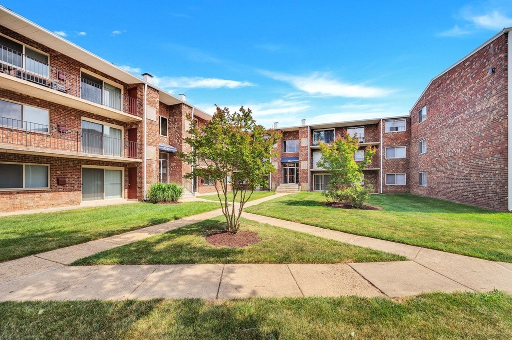 a grassy area with trees in front of an apartment building