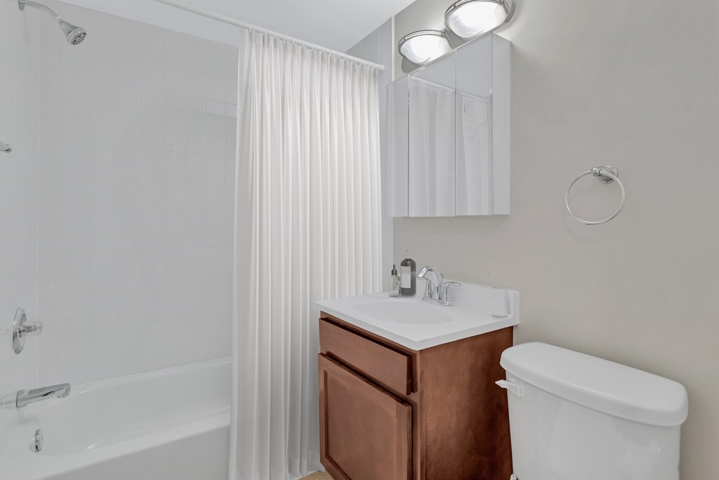 A white bathroom with a brown vanity and a white toilet.