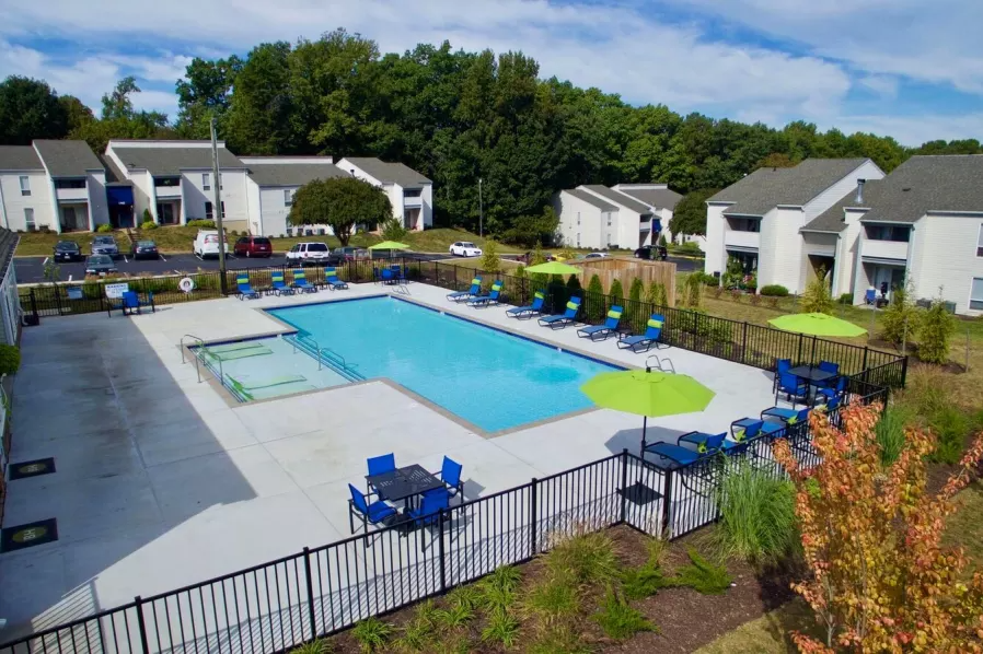 a swimming pool with chairs and umbrellas in front of apartment buildings