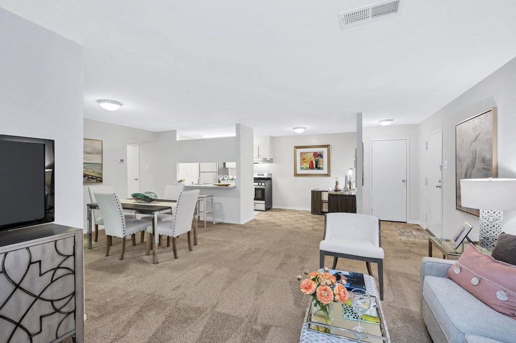 a living room and dining area with a television and kitchen in the background