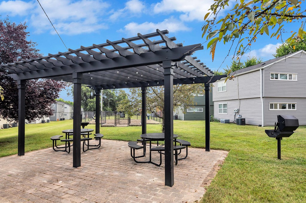 a pergola with picnic tables on a brick patio