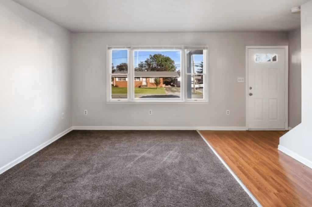 an empty living room with a large window and wooden floors